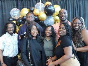 A group of men and women smiling in front of graduation themed balloons 